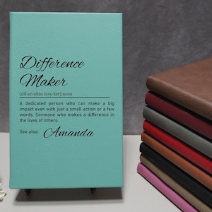 May include: A teal leather-bound journal with the word "Difference Maker" and a definition of the word. The name "Amanda" is written below the definition.