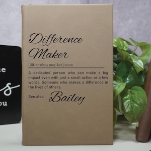 May include: A tan leather-bound journal with the word "Difference Maker" printed on the front. The definition of the word is printed below, along with the name "Bailey".