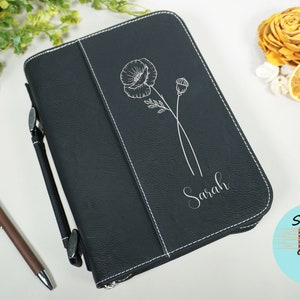 Op de afbeelding: Zwarte leren bijbelhoes met witte stiksels. De hoes heeft een zilveren gegraveerde klaproos en de naam "Sarah".
