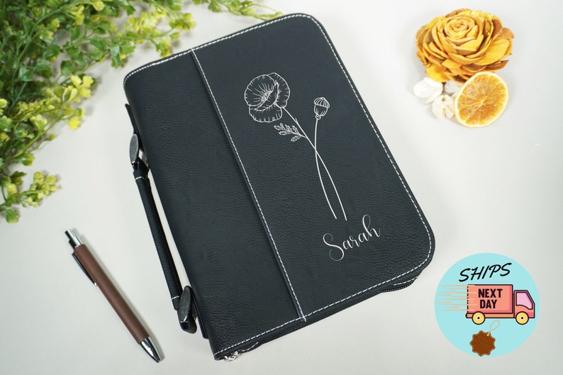 Op de afbeelding: Zwarte leren bijbelhoes met witte stiksels. De hoes heeft een zilveren gegraveerde klaproos en de naam "Sarah".