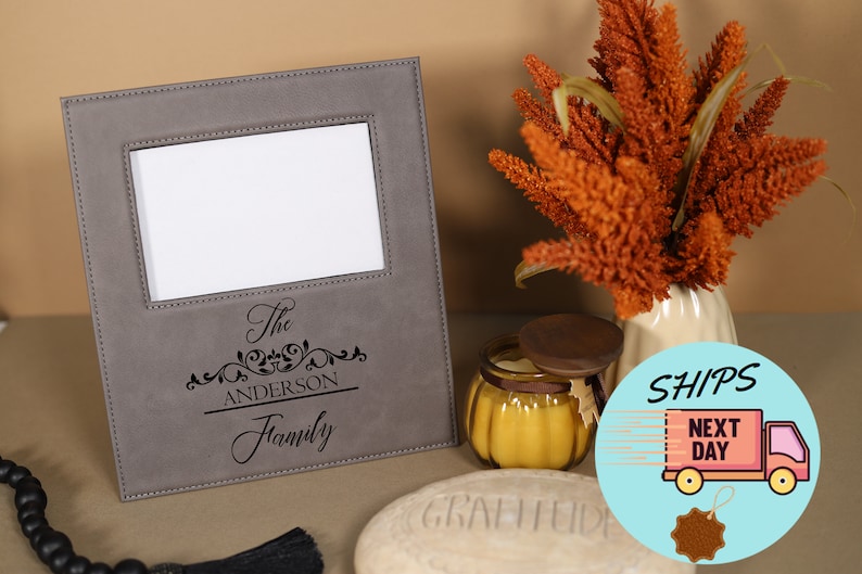 May include: A gray faux leather picture frame with a white mat and a black engraved inscription that reads "The Anderson Family".