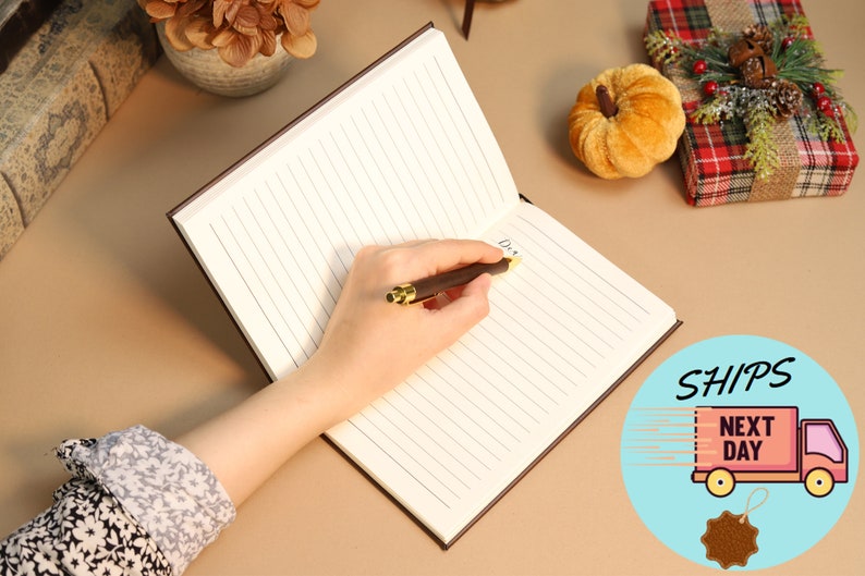 May include: A brown leather-bound journal with lined pages. A person is writing in the journal with a gold-tipped pen. The journal is open to a blank page.