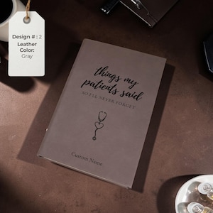 K&ouml;nnte beinhalten: Graues Lederjournal mit dem Text "things my patients said SO I'LL NEVER FORGET" und einer Stethoskop-Grafik. Das Journal bietet auch Platz f&uuml;r einen individuellen Namen. Ein Etikett zeigt die Designnummer und die Lederfarbe an.