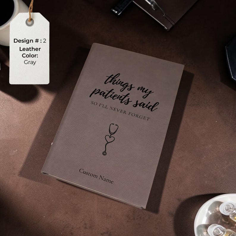 K&ouml;nnte beinhalten: Graues Lederjournal mit dem Text "things my patients said SO I'LL NEVER FORGET" und einer Stethoskop-Grafik. Das Journal bietet auch Platz f&uuml;r einen individuellen Namen. Ein Etikett zeigt die Designnummer und die Lederfarbe an.
