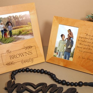 May include: Two wooden picture frames with a quote about family. The frame on the left has a photo of a family of four walking on a path in a field. The frame on the right has a photo of a family of three standing in a field. The quote reads, "It is more important than ever to make our families the center of our lives and the top of our priorities." - L. Tom Perry.