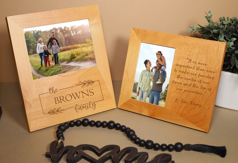 May include: Two wooden picture frames with a quote about family. The frame on the left has a photo of a family of four walking on a path in a field. The frame on the right has a photo of a family of three standing in a field. The quote reads, "It is more important than ever to make our families the center of our lives and the top of our priorities." - L. Tom Perry.