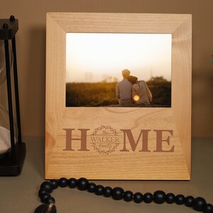 May include: A wooden picture frame with a photo of a couple sitting on a hill at sunset. The frame is engraved with the words "HOME" and "The Walker Family".