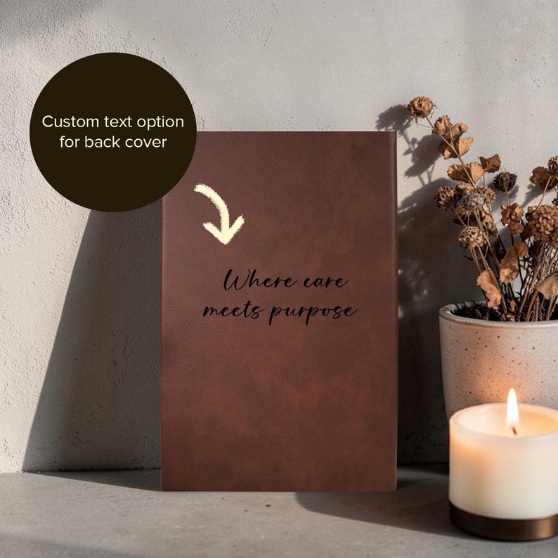 K&ouml;nnte beinhalten: Ein braunes Notizbuch mit dem Text "Where care meets purpose" auf dem Einband. Eine Option f&uuml;r individuellen Text f&uuml;r die R&uuml;ckseite ist ebenfalls verf&uuml;gbar. Das Notizbuch wird neben einer brennenden Kerze und einer dekorativen Pflanze pr&auml;sentiert.