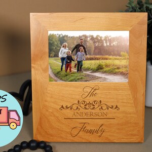 May include: A wooden photo frame with a light brown finish. The frame has a 4x6 inch opening and features an engraved design with the text "The Anderson Family".
