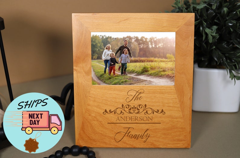 May include: A wooden photo frame with a light brown finish. The frame has a 4x6 inch opening and features an engraved design with the text "The Anderson Family".