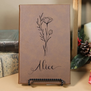 May include: A brown leather journal with a floral design and the name "Alice" engraved on the front.