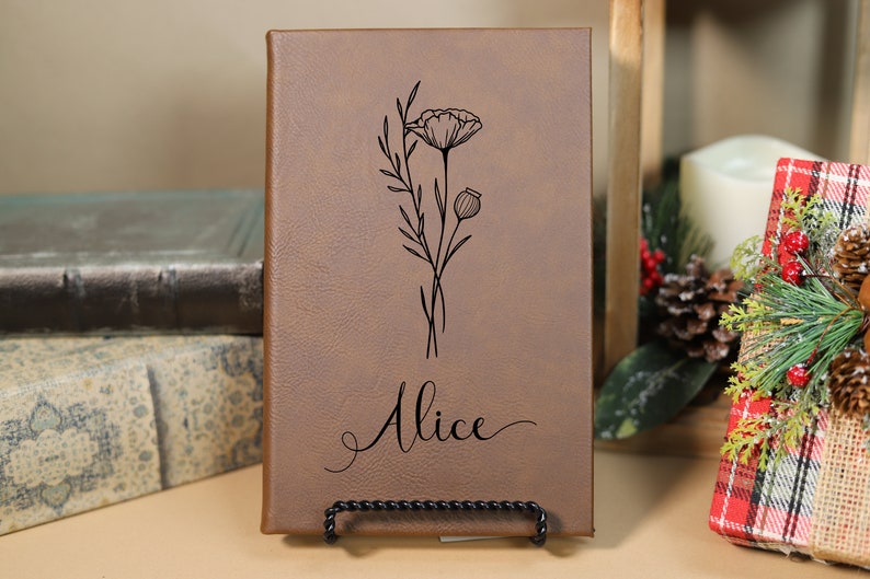 May include: A brown leather journal with a floral design and the name "Alice" engraved on the front.