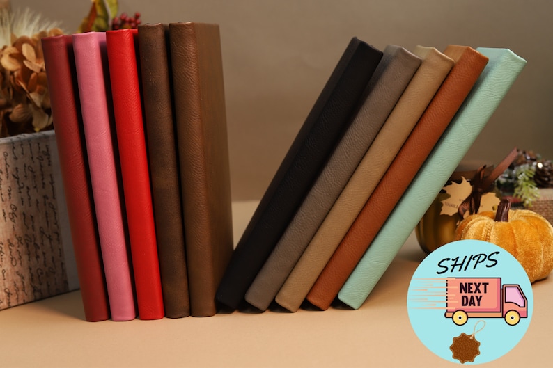 May include: A collection of ten leather-bound journals in various colors, including pink, red, brown, black, gray, beige, orange, and blue. The journals are arranged in a staggered pattern, with the blue journal at the front.