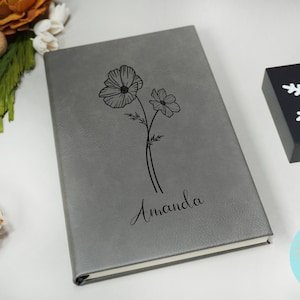 May include: A gray faux leather journal with a floral design and the name "Amanda" engraved on the front.