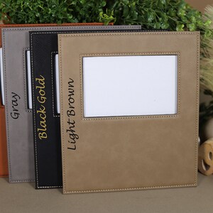 May include: Four leather picture frames in different colors: rawhide, gray, black gold, and light brown. Each frame has a stitched border and a small window for a photo.