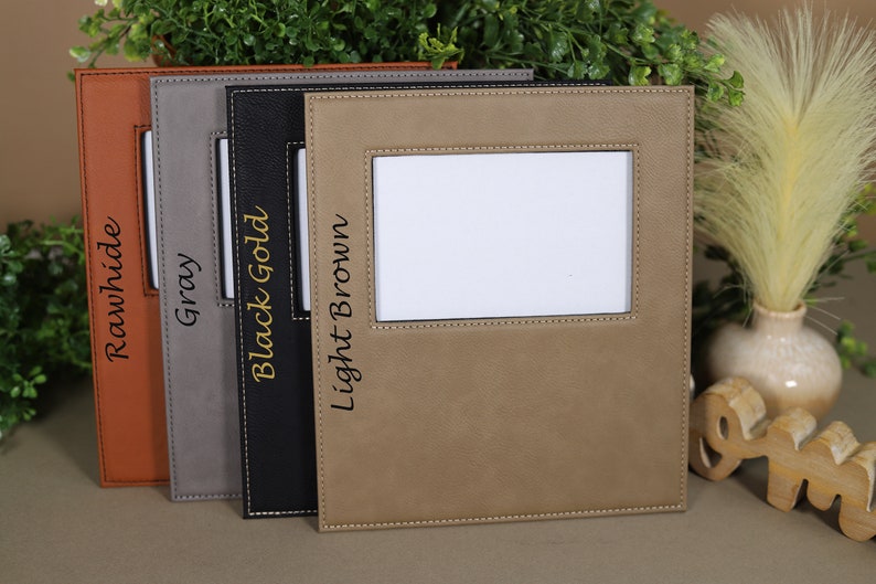 May include: Four leather picture frames in different colors: rawhide, gray, black gold, and light brown. Each frame has a stitched border and a small window for a photo.