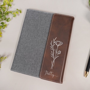 May include: A brown leather journal with a gray fabric cover. The front cover has a floral design and the name "Patty" engraved on it.