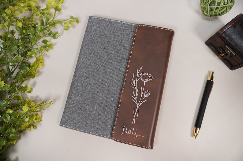 May include: A brown leather journal with a gray fabric cover. The front cover has a floral design and the name "Patty" engraved on it.