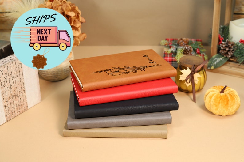 May include: A stack of five brown, red, black, gray, and beige leather journals with a floral design and the word "Journal" engraved on the top journal.