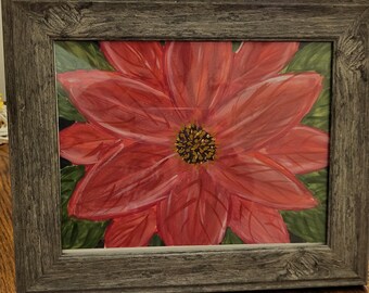 May include: A framed painting of a red poinsettia flower with green leaves. The flower has a yellow and brown center. The frame is a weathered gray color. The artwork is displayed on a wooden surface.