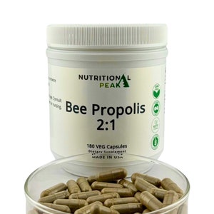 May include: A white plastic jar with a green label that reads "Nutritional Peak Bee Propolis 2:1 180 VEG Capsules Dietary Supplement Made in USA". The jar is filled with brown capsules and is sitting on a clear glass plate.