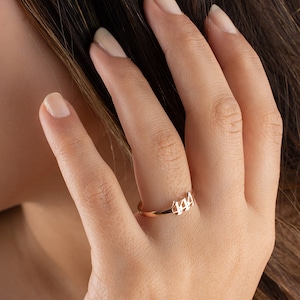 May include: A delicate gold ring featuring the number "444" in a minimalist design. The ring is worn on a finger, showcasing its slender band and the subtle, yet meaningful, numerical detail. The ring's warm gold tone contrasts with the skin.