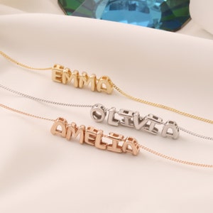 Könnte beinhalten: Drei Halsketten mit Namen in Blockbuchstaben. Die Namen sind "EMMA" in Gold, "OLIVIA" in Silber und "AMELIA" in Roségold. Jede Halskette hat eine zarte Kette.
