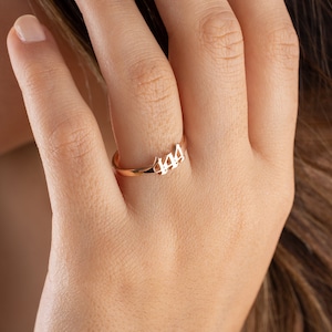 May include: A rose gold ring with the number 444 cut out in a delicate font. The ring is shown on a person's finger, highlighting its simple yet elegant design. The ring is a piece of jewelry.