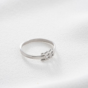 May include: A silver ring with a geometric design. The ring features a thin band and a decorative element composed of interconnected shapes. The ring is displayed on a white surface, highlighting its metallic sheen.