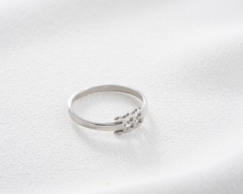 May include: A silver ring with a geometric design. The ring features a thin band and a decorative element composed of interconnected shapes. The ring is displayed on a white surface, highlighting its metallic sheen.