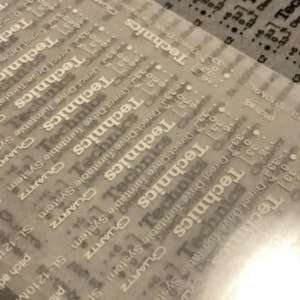 May include: A close-up of a translucent overlay featuring the word "Technics" in a repeating pattern. The text "Direct Drive Turntable System" and "SL-1210MK2" are also visible. The overlay has a grid-like design.