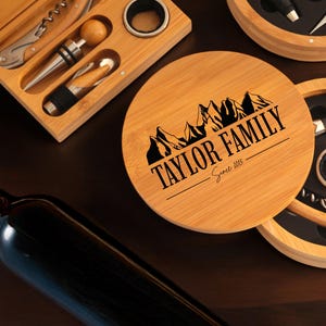May include: A wooden box with a lid that has the text "TAYLOR FAMILY Since 1985" engraved on it. The box contains a wine opener, a bottle stopper, a foil cutter, and a ring puller. The box is made of bamboo and has a natural wood finish.