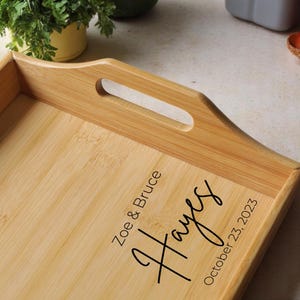 May include: A rectangular bamboo serving tray with a handle cutout. The tray is engraved with the names "Zoe & Bruce Hayes" and the date "October 23, 2023" in black script. The tray is light brown.