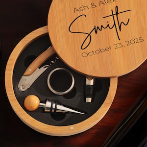May include: A wooden box with a lid that opens to reveal a wine opener, a bottle stopper, and a foil cutter. The lid is engraved with the text "Ash & Alex Smith October 23, 2025".