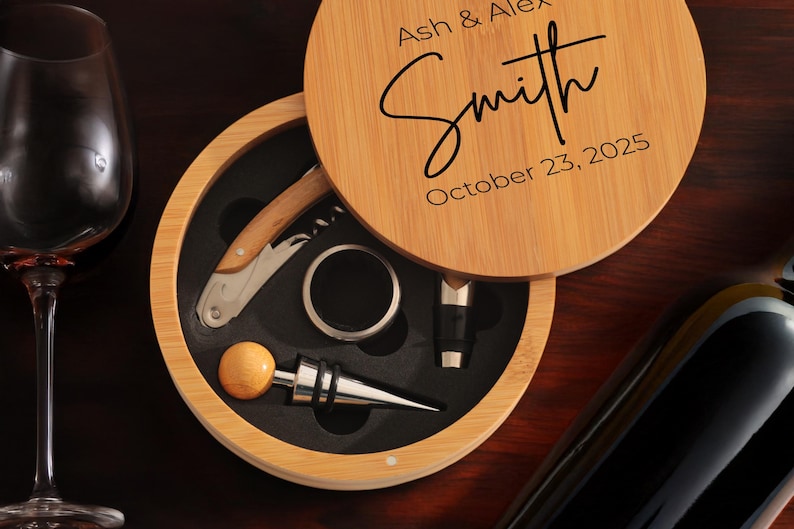 May include: A wooden box with a lid that opens to reveal a wine opener, a bottle stopper, and a foil cutter. The lid is engraved with the text "Ash & Alex Smith October 23, 2025".