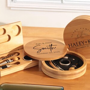 May include: Two wooden boxes with engraved text. One box is round and has the text "Haley + Kyle" and "December 12, 2022". The other box is rectangular and has the text "Ash & Alex Smith" and "October 23, 2025".