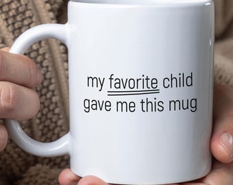 May include: White ceramic mug with black text that reads "my favorite child gave me this mug". The word "favorite" is crossed out.