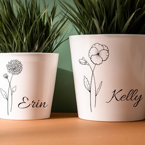 May include: Two white ceramic flower pots with black floral designs and personalized names. The pot on the left says "Erin" and the pot on the right says "Kelly".