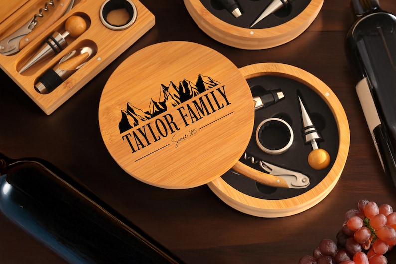 May include: A wooden box with a lid that has the text "TAYLOR FAMILY Since 1985" engraved on it. The box contains a wine opener, a bottle stopper, a foil cutter, and a ring puller. The box is made of bamboo and has a natural wood finish.