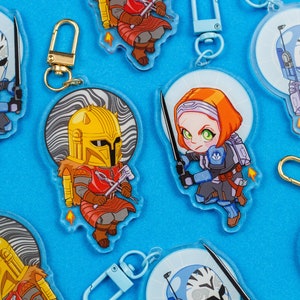 May include: A set of six colourful keychains featuring cartoon characters wearing helmets and armour. The keychains are made of clear acrylic and have a swirl pattern in the background. The characters are in various poses, including holding weapons and standing in a fighting stance.