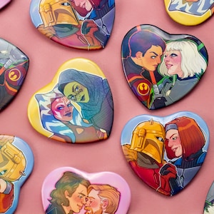 May include: A set of heart-shaped pins featuring various couples from the Star Wars universe. The pins are colorful and feature characters like Ahsoka Tano, Sabine Wren, and Rex.