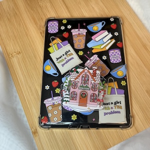 May include: Black tablet case with a colorful design featuring a bookstore, coffee cups, books, strawberries, and the text "Just a girl with a TBR problem." The case has a clear border.