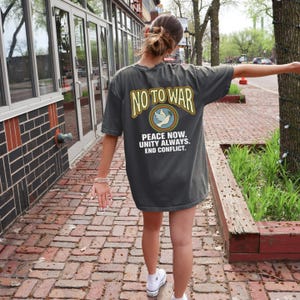 May include: Dark gray t-shirt with the text "NO TO WAR" in yellow and a peace dove graphic. The shirt also features the phrases "PEACE NOW. UNITY ALWAYS. END CONFLICT."