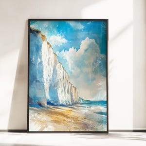 May include: A framed watercolour print showing white cliffs under a blue sky with clouds. The coastal landscape features a sandy beach and the sea. The black-framed artwork is displayed against a white wall, capturing a serene seaside scene.