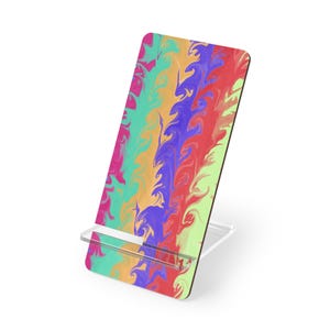 May include: A rectangular phone stand featuring a vibrant, multi-colored marbled pattern with swirling streaks of magenta, turquoise, orange, deep purple, red, and light green. The stand is constructed from a flat, upright panel supported by a clear base.