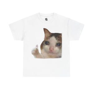 Puede incluir: Camiseta blanca con una imagen impresa de un gato dando un pulgar hacia arriba con una expresi&oacute;n triste. El gato tiene pelaje marr&oacute;n, blanco y naranja.