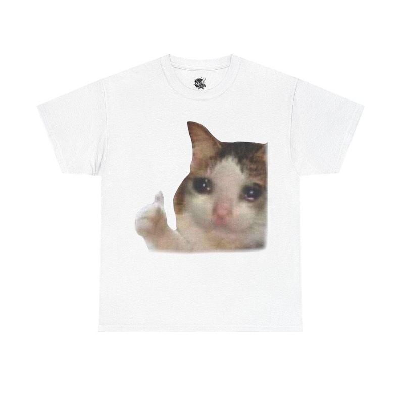 Puede incluir: Camiseta blanca con una imagen impresa de un gato dando un pulgar hacia arriba con una expresi&oacute;n triste. El gato tiene pelaje marr&oacute;n, blanco y naranja.