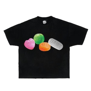 May include: Black t-shirt with a graphic of colourful sweets. The design includes a pink heart-shaped sweet with "YOU", a green round sweet with "NEED", an orange round sweet with "ME", and a white pill-shaped sweet with "BABY".