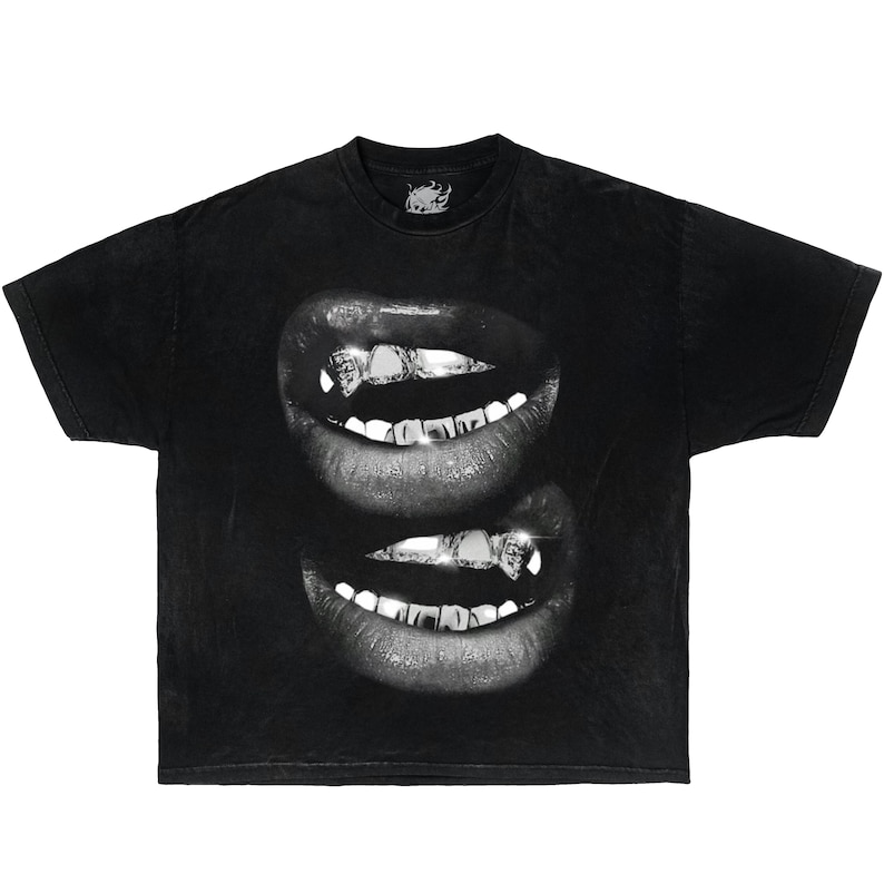 May include: A black short-sleeve t-shirt featuring a graphic print of two sets of lips stacked vertically. The lips are rendered in grayscale and show teeth adorned with metallic, diamond-like grillz that catch the light.