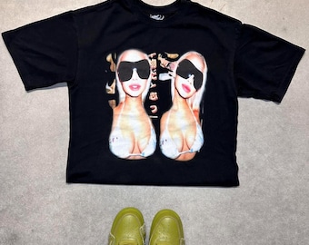 May include: Black t-shirt with a graphic print of two women wearing sunglasses and bikinis. The women are smiling and looking at the camera.